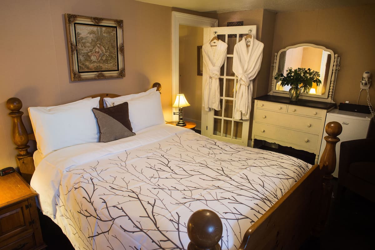 Un dormitorio con cama, mesita de noche, cómoda, espejo y puerta que da a un baño.