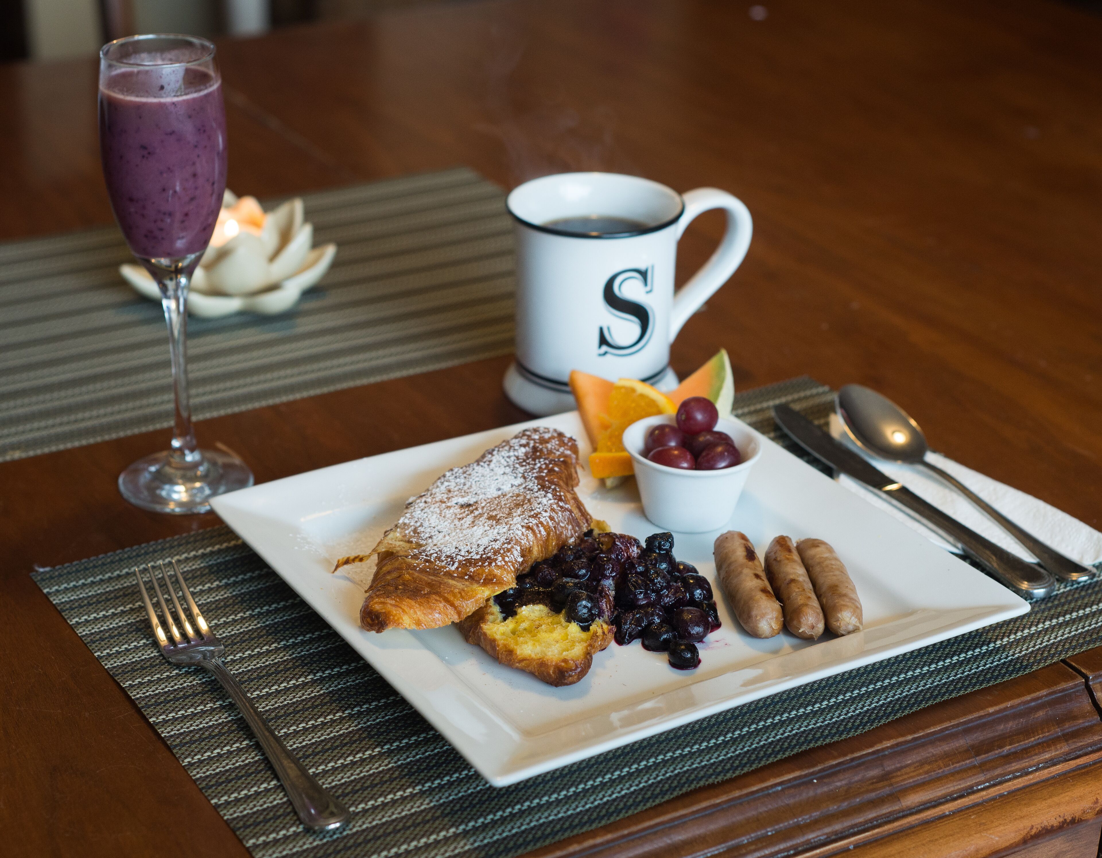 A breakfast plate with toast, berries, sausages, and a cup of coffee on a wooden table.