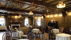 A cozy dining area with round tables and chairs, string lights, and a fireplace. - Stevenson Inn & Spa (Essa)