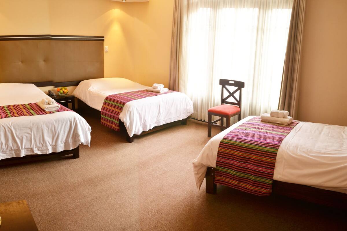 A hotel room with two single beds, a chair, a nightstand, and a decorative vase.
