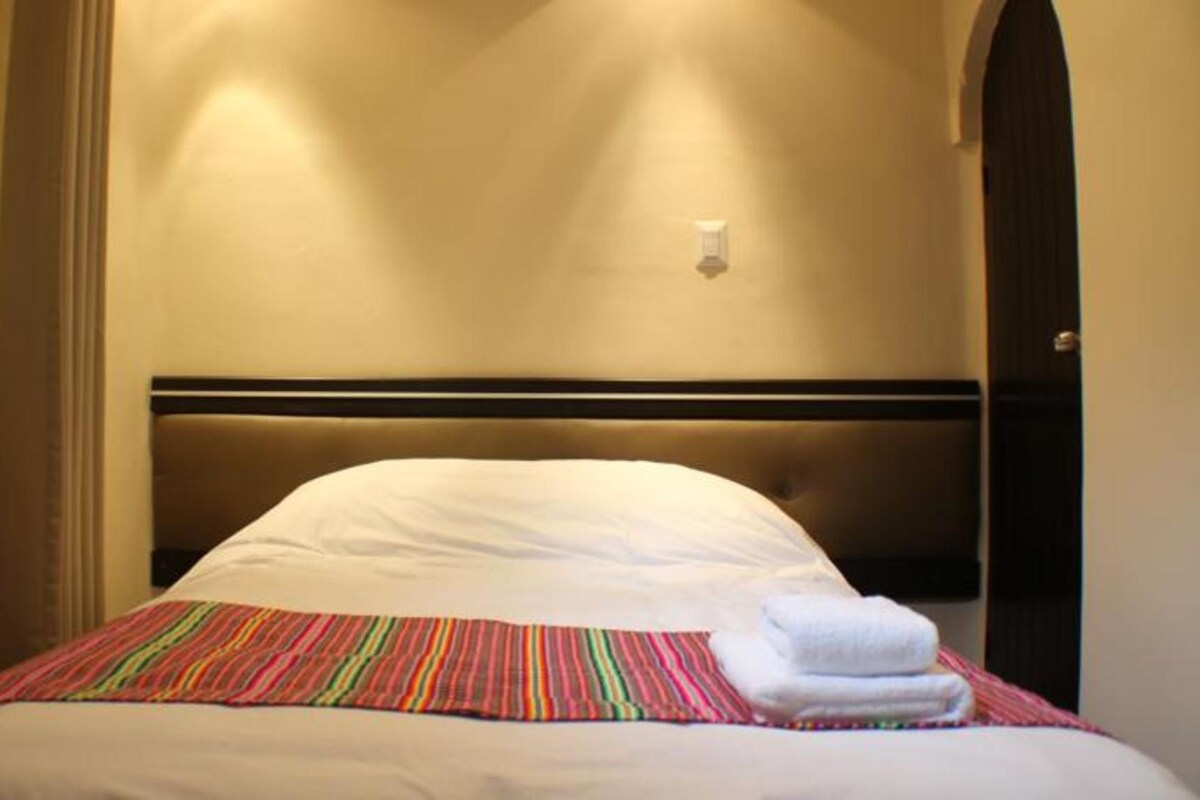 A hotel room with a bed, a striped blanket, and a white pillow.