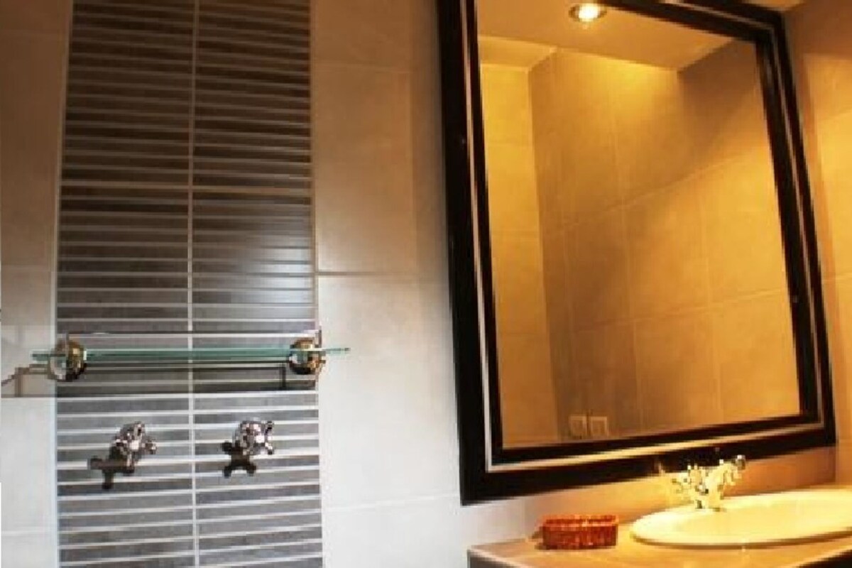 Un baño con un espejo grande, un lavamanos y un perchero para toallas.