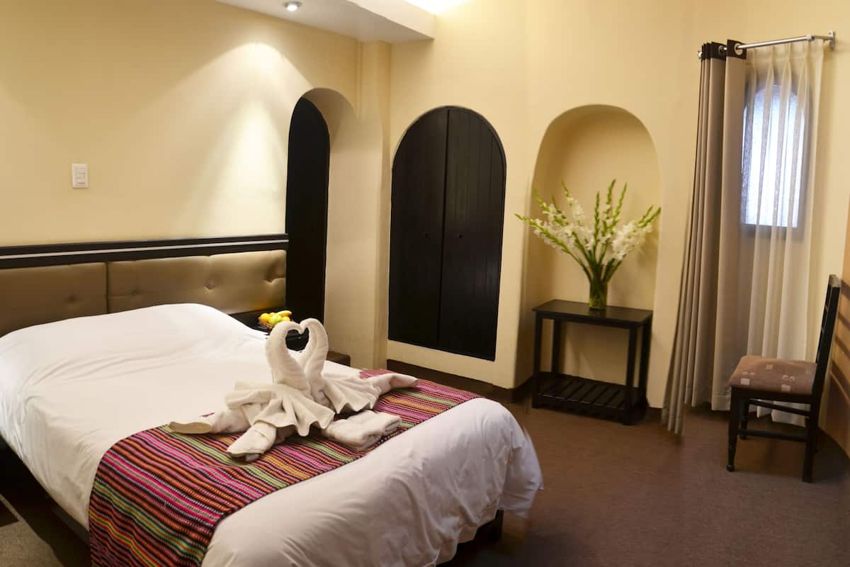 A hotel room with a large bed, a small table with a vase of flowers, and a chair.