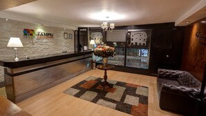 Un área de recepción con un mostrador de madera, una lámpara de araña, un tapete estampado y un sillón de cuero.
