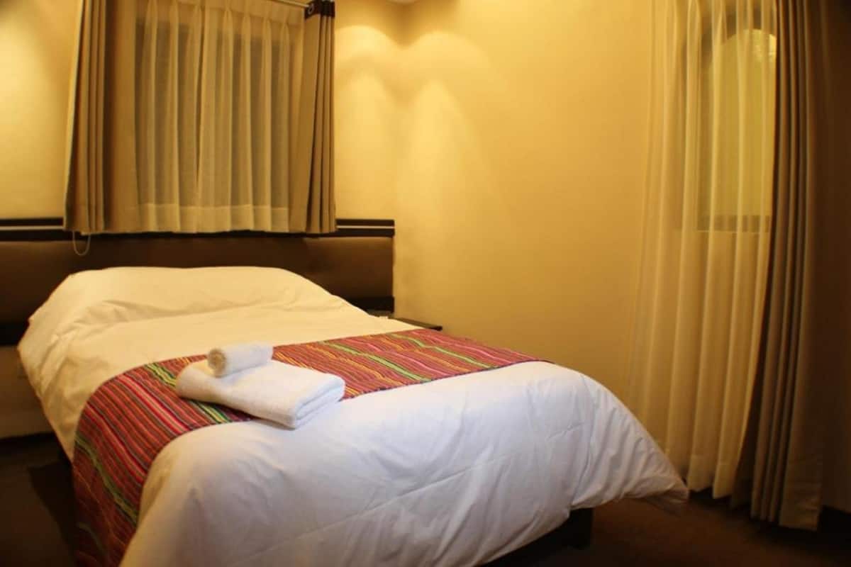 A hotel room with a bed, beige curtains, and a striped bedspread.