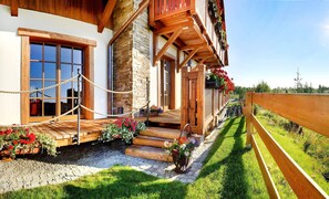 A rustic wooden house with a stone facade, wooden steps leading to a porch, and a rope barrier. - panoraMic Mountain Residence (Vysoké Tatry)