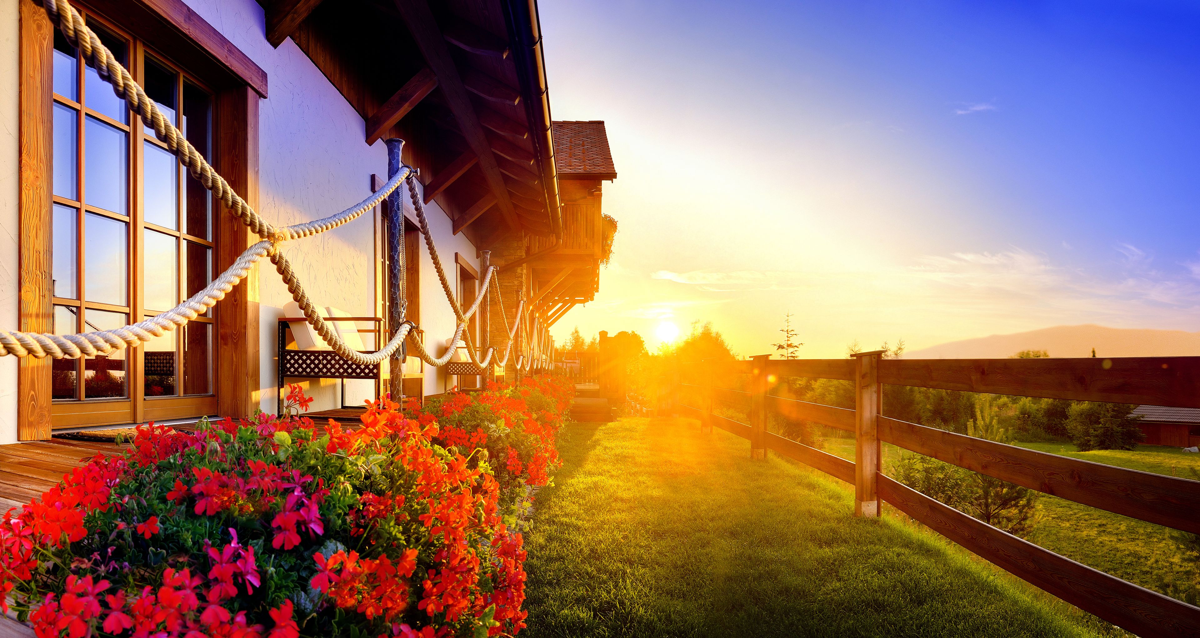 A wooden building with a rope barrier, a wooden deck, and a grassy area with flowers.