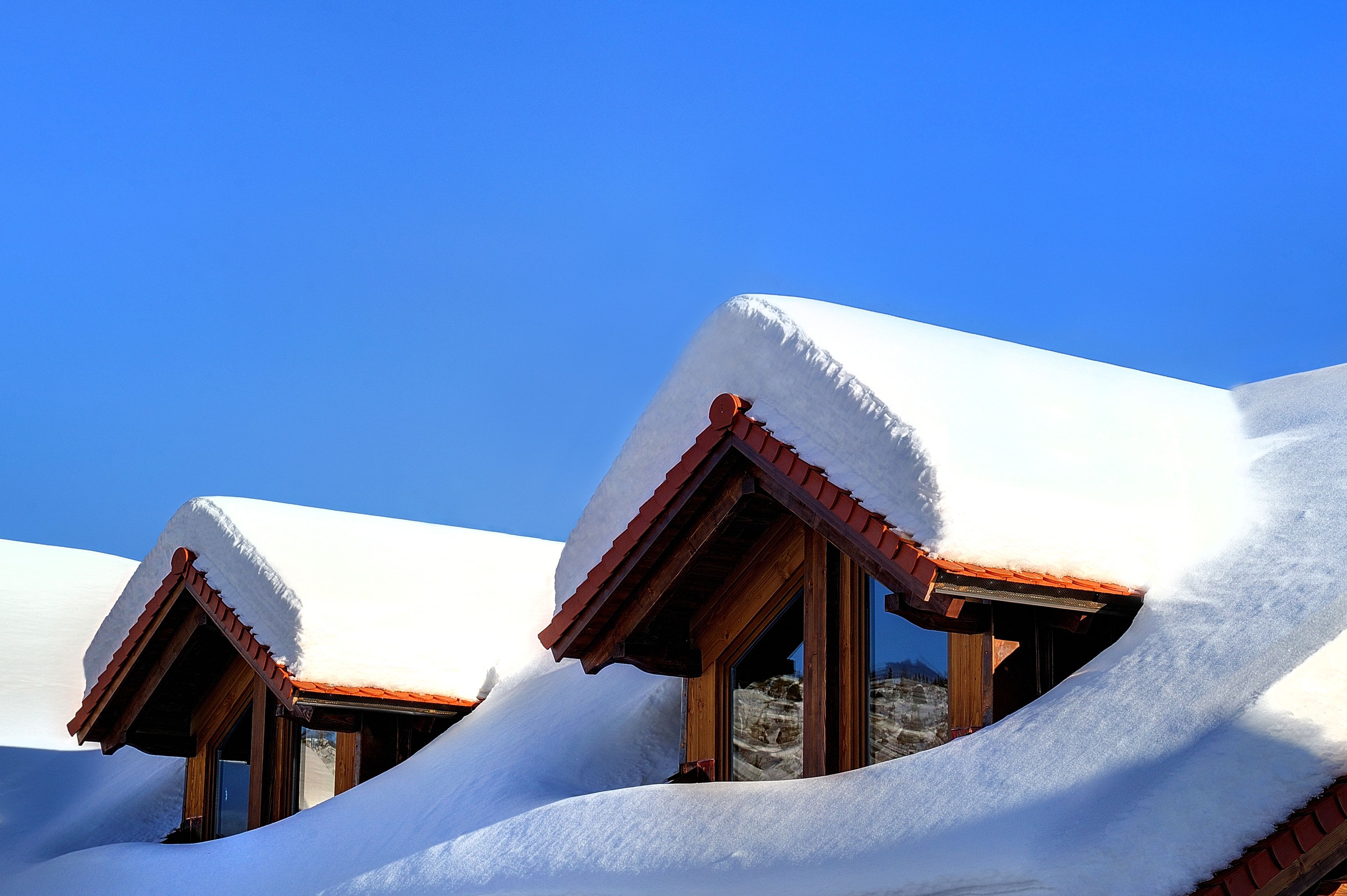 A row of chalet-style buildings with steeply pitched roofs covered in snow, set against a clear blue sky.