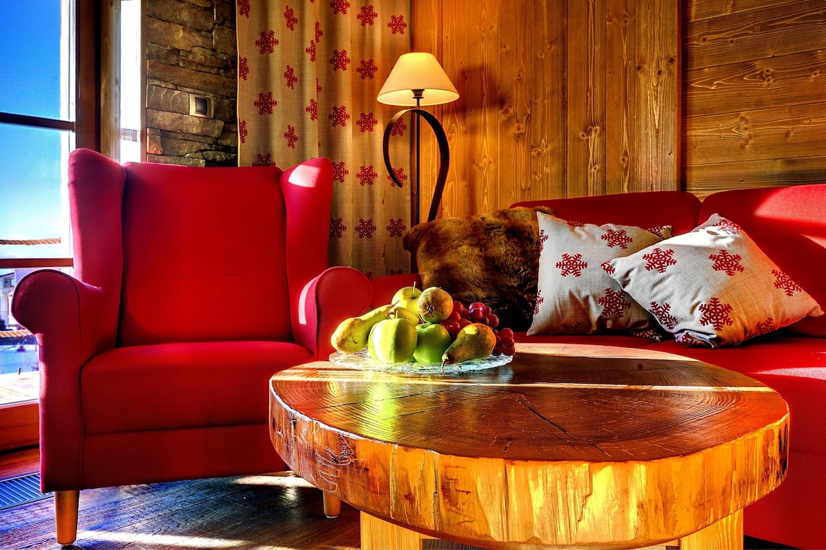 Een gezellige kamer met een rode bank, een houten bijzettafeltje met fruit en een lamp.