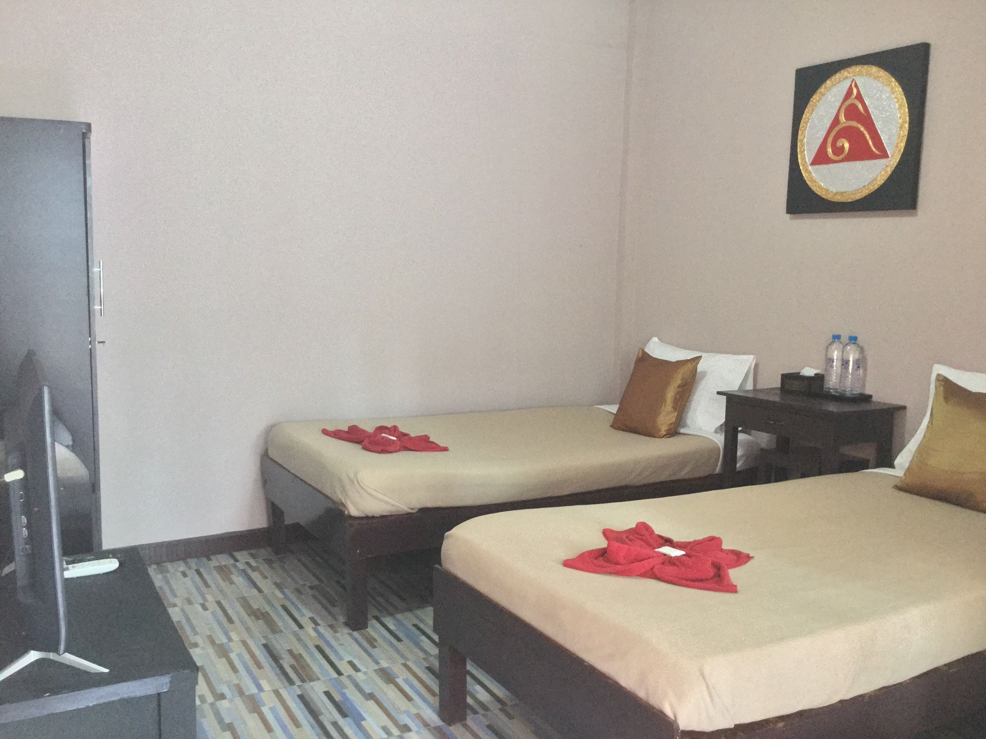A hotel room with two single beds, a desk, a chair, a television, and a water bottle on the desk.