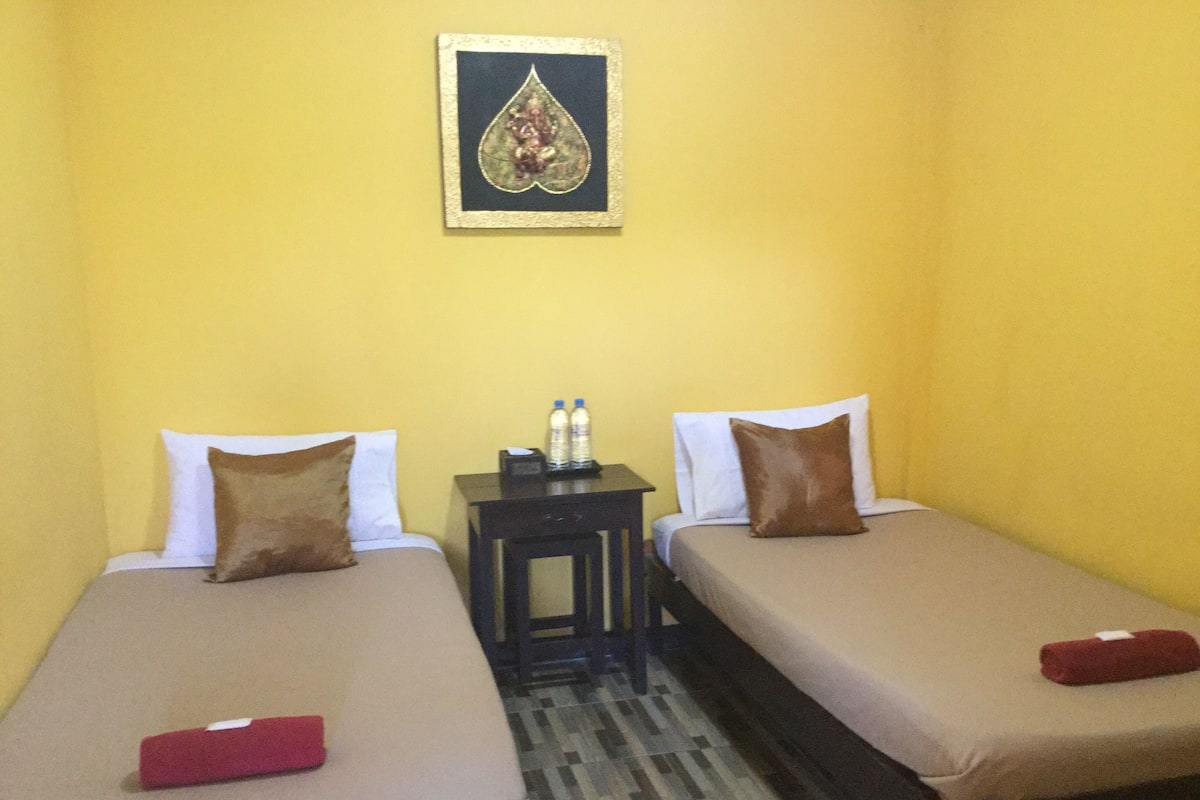 A hotel room with two single beds, each with a pillow and a red towel. There is a small table with two water bottles on it.