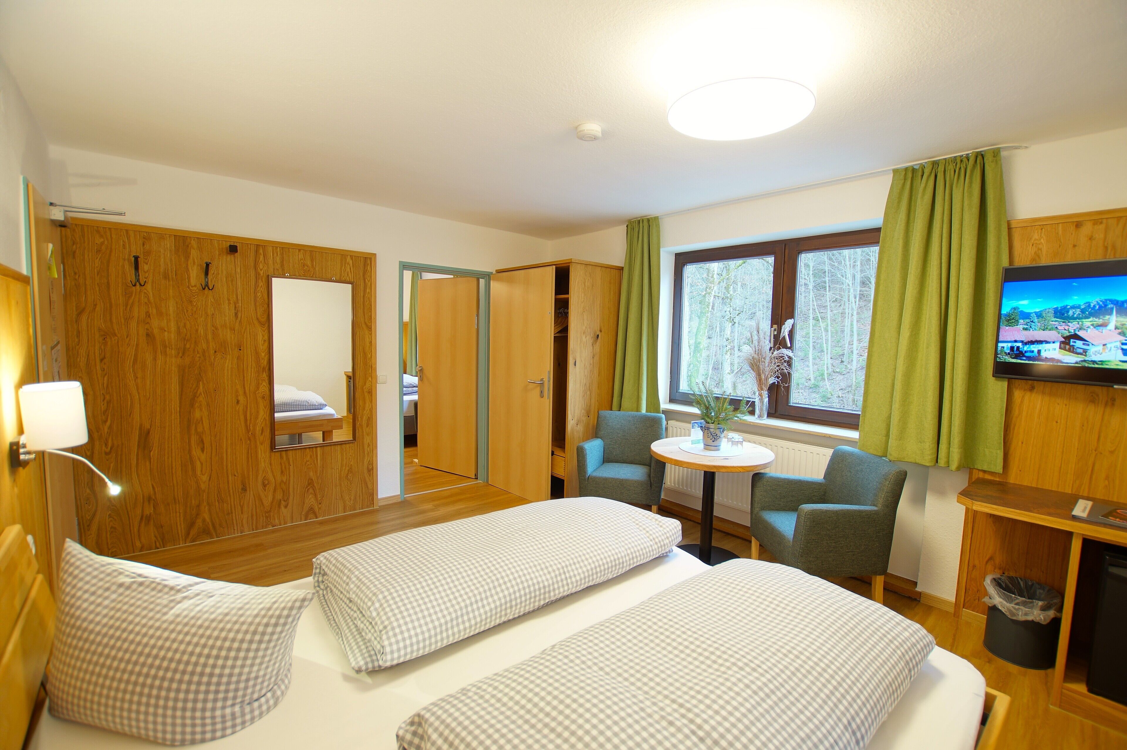 A hotel room with two beds, a small table, two chairs, a TV, and a window with curtains.