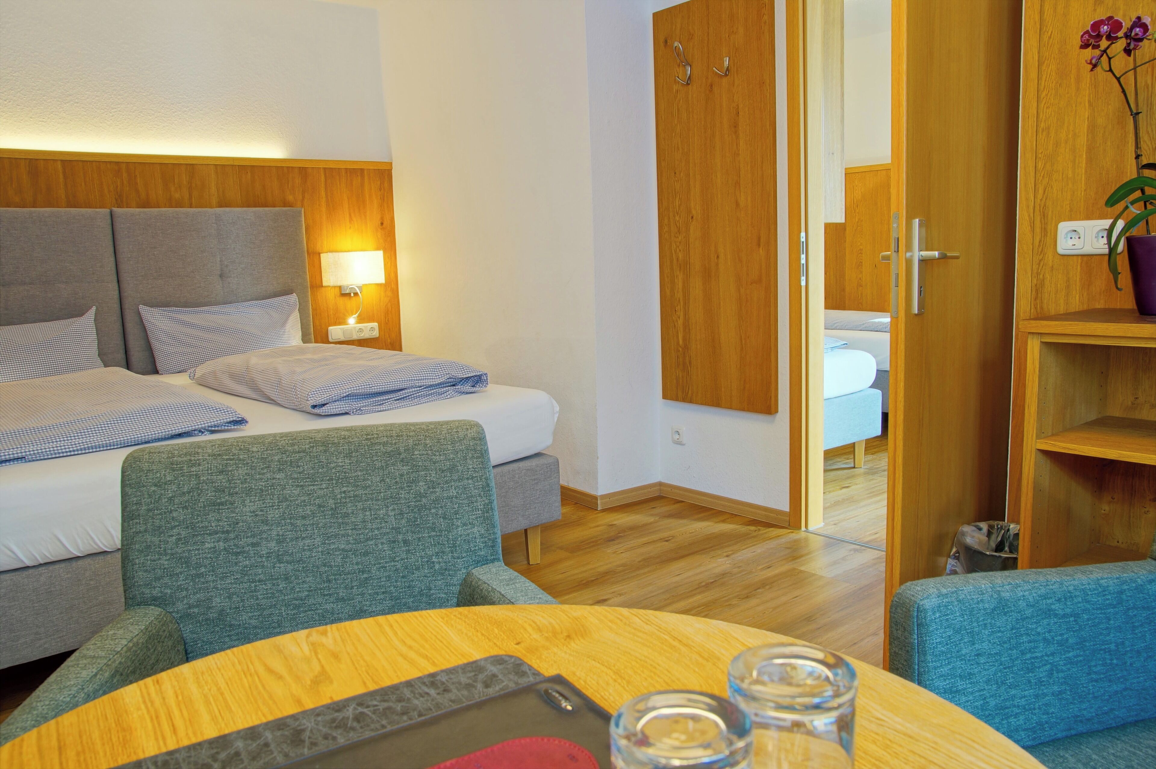 A hotel room with a bed, two chairs, a table, a wardrobe, and a potted plant.
