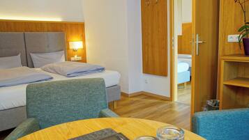 A hotel room with a bed, two chairs, a table, a wardrobe, and a potted plant.