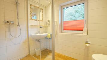 A bathroom with a glass-enclosed shower, a sink, a toilet, and a window with blinds.