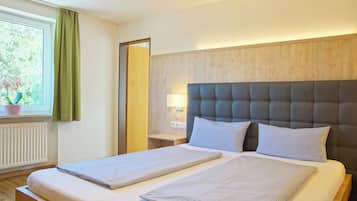 Una cama bien hecha con cabecera, una mesita de noche con lámpara y una ventana con cortinas.