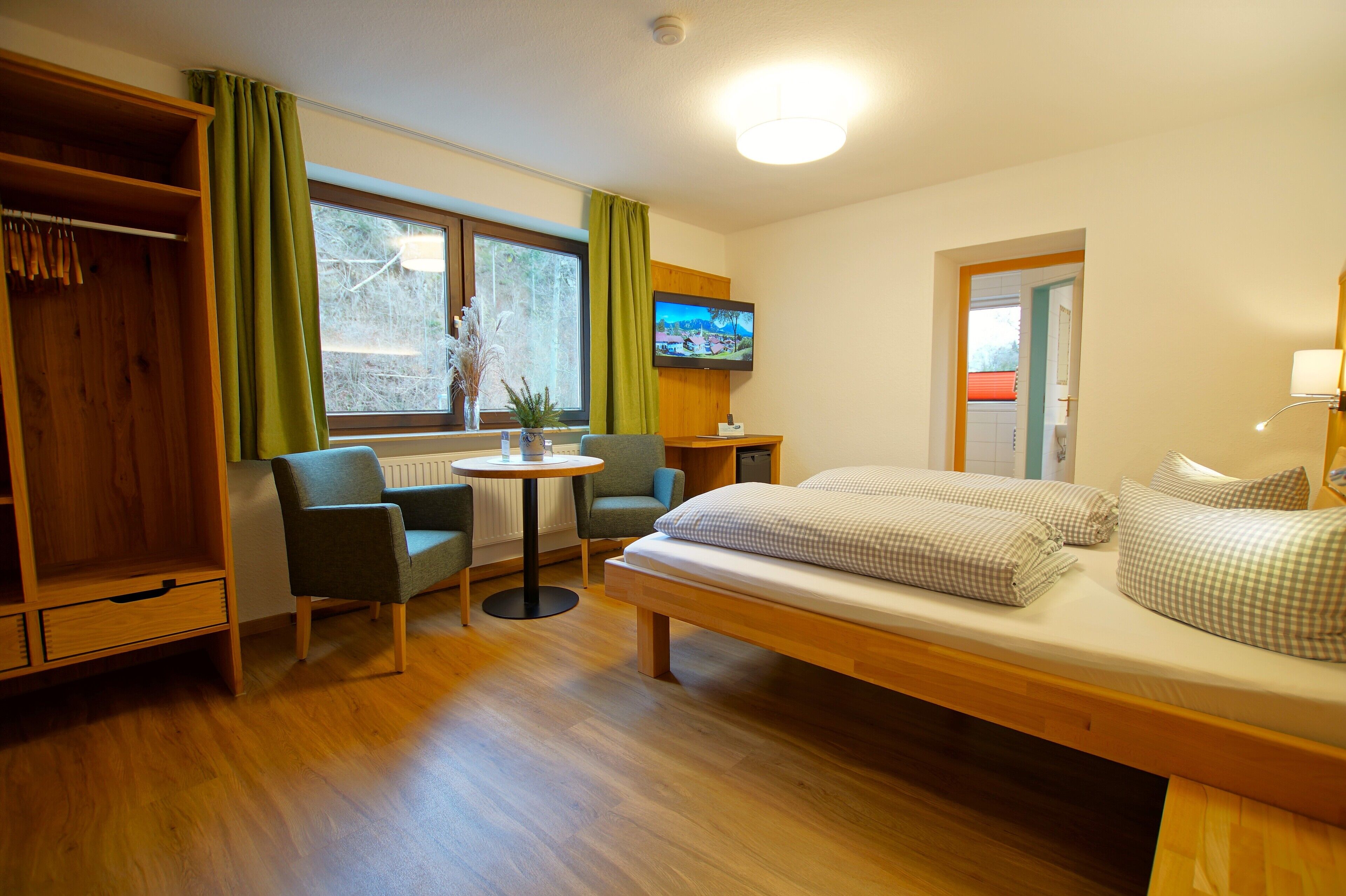 Ett litet rum med en säng, två stolar, ett litet bord, en tv och en garderob.