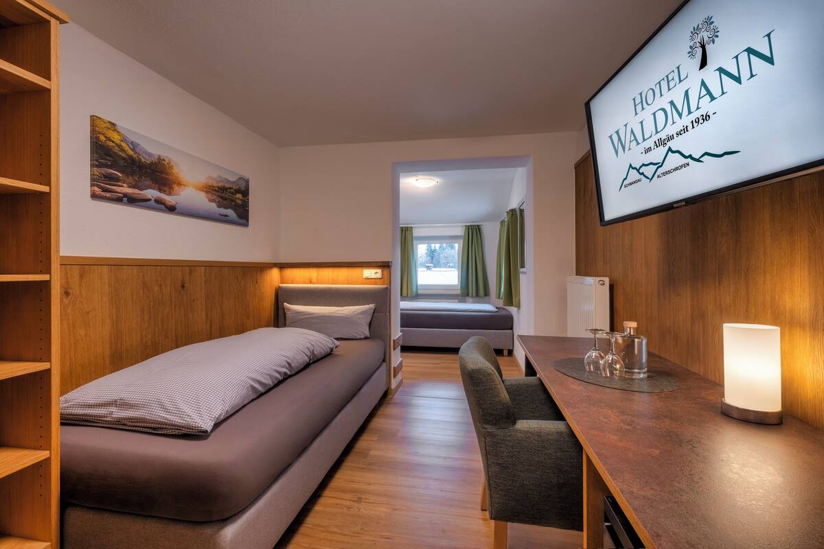 Hotellihuone, jossa on sänky, työpöytä tuolilla, televisio ja taulu seinällä.