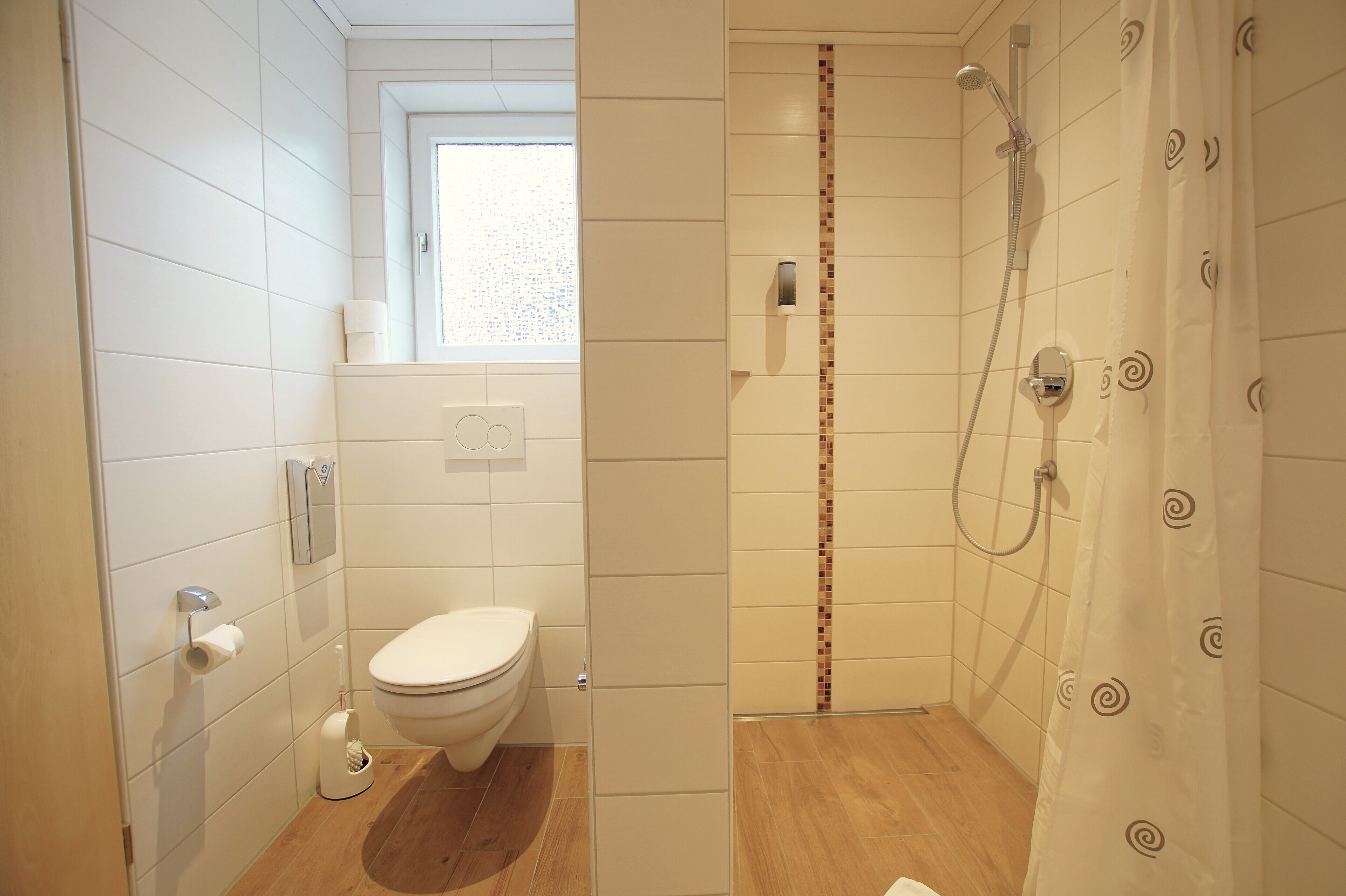 A modern bathroom with a toilet, shower, and a window.
