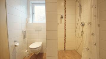 A modern bathroom with a toilet, shower, and a window.