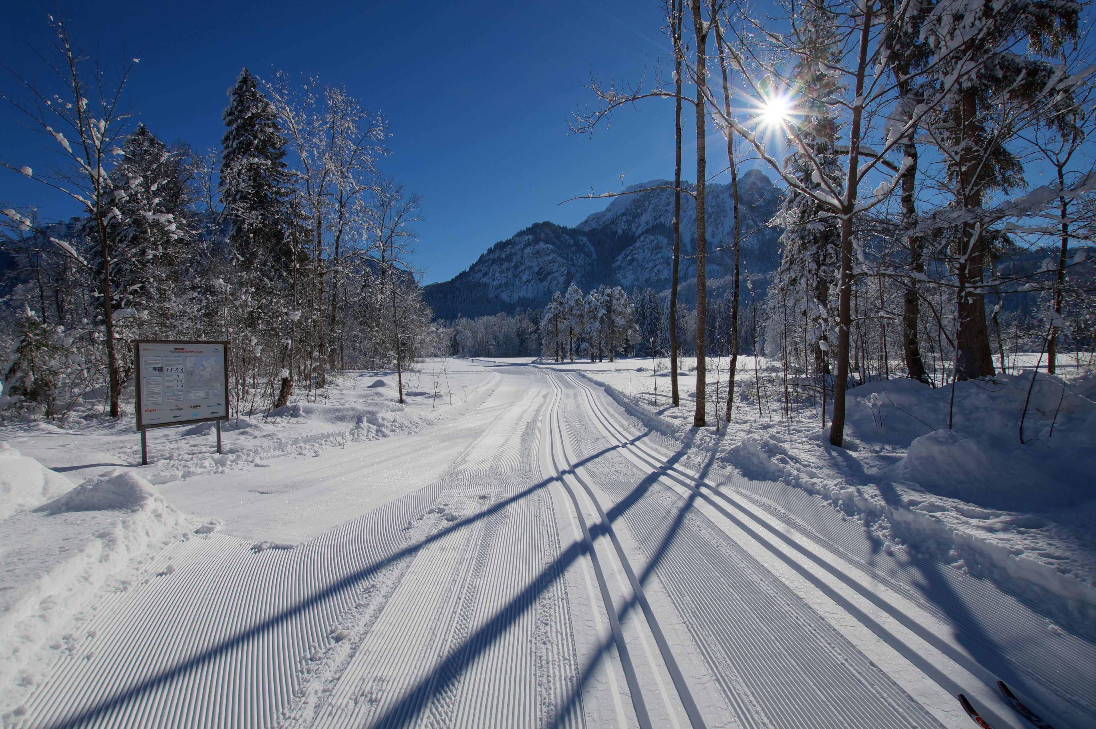 A snow-covered road with a signpost, surrounded by trees and mountains.