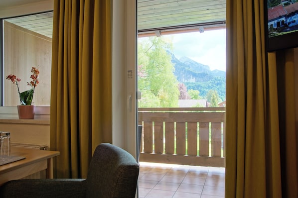 Une chambre avec vue sur les montagnes, un balcon avec une balustrade en bois, une chaise, une table et une plante en pot.