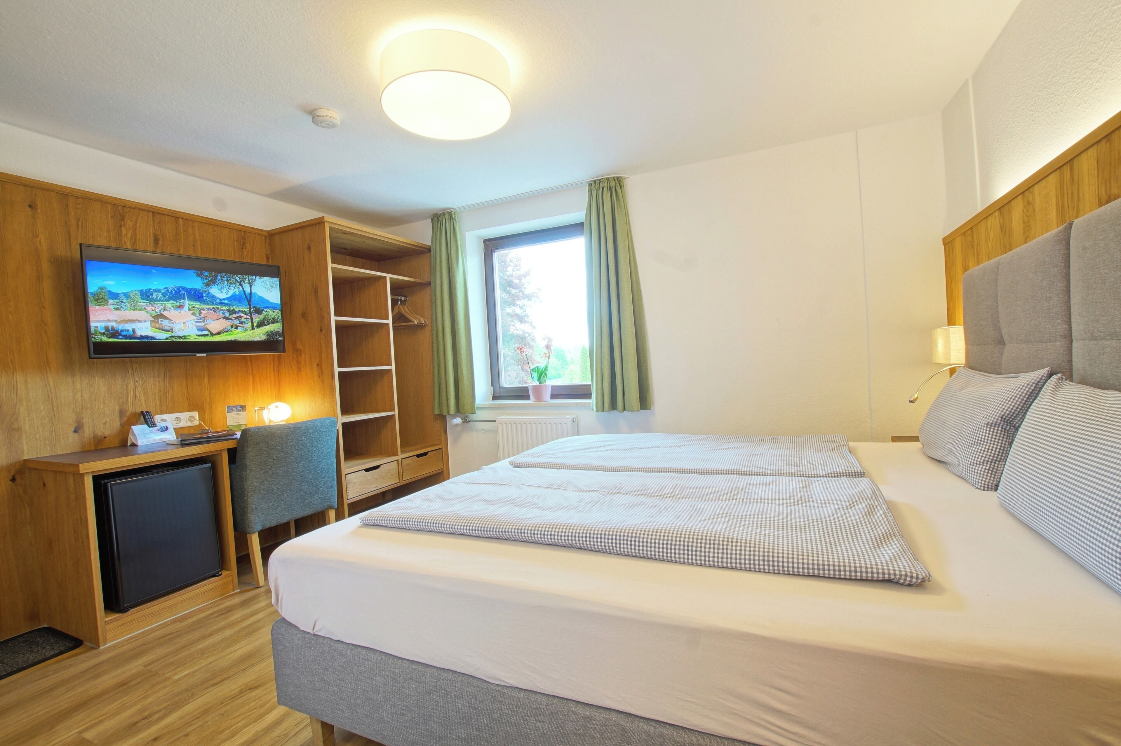 Een hotelkamer met een bed, een bureau met een computer, een televisie en een raam met gordijnen.