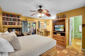 A bedroom with a large bed, a ceiling fan, a fireplace, a television, and a bookshelf.