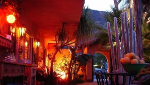 An outdoor area with a thatched roof, palm trees, and a seating area with a bowl of fruit. - Coyote Inn - 21 and Over - A Town & Desert Boutique Hotel (Palm Springs)