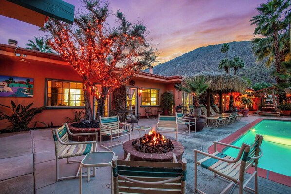 A poolside area with a fire pit, lounge chairs, and a building with a mountain backdrop.