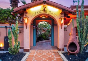 The entrance to Coyote Inn with a distinctive arched doorway, illuminated by wall-mounted lights, and surrounded by cacti and a decorative pot.