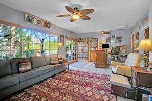 A living room with a sofa, armchairs, a patterned rug, a ceiling fan, and a bookshelf.