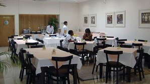 A dining area with multiple tables and chairs, a kitchen in the background, and framed pictures on the walls. - VIP Inn Beira (Beira)