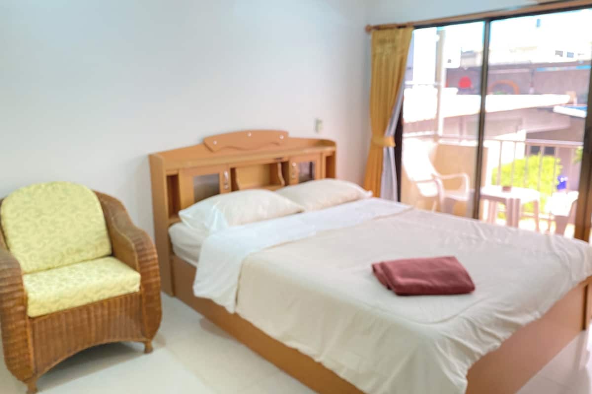 Una habitación de hotel con una cama, una silla y un ventanal con cortinas.