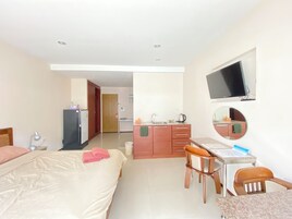 Una habitación de hotel con cama, escritorio, sillas, televisor y kitchenette.