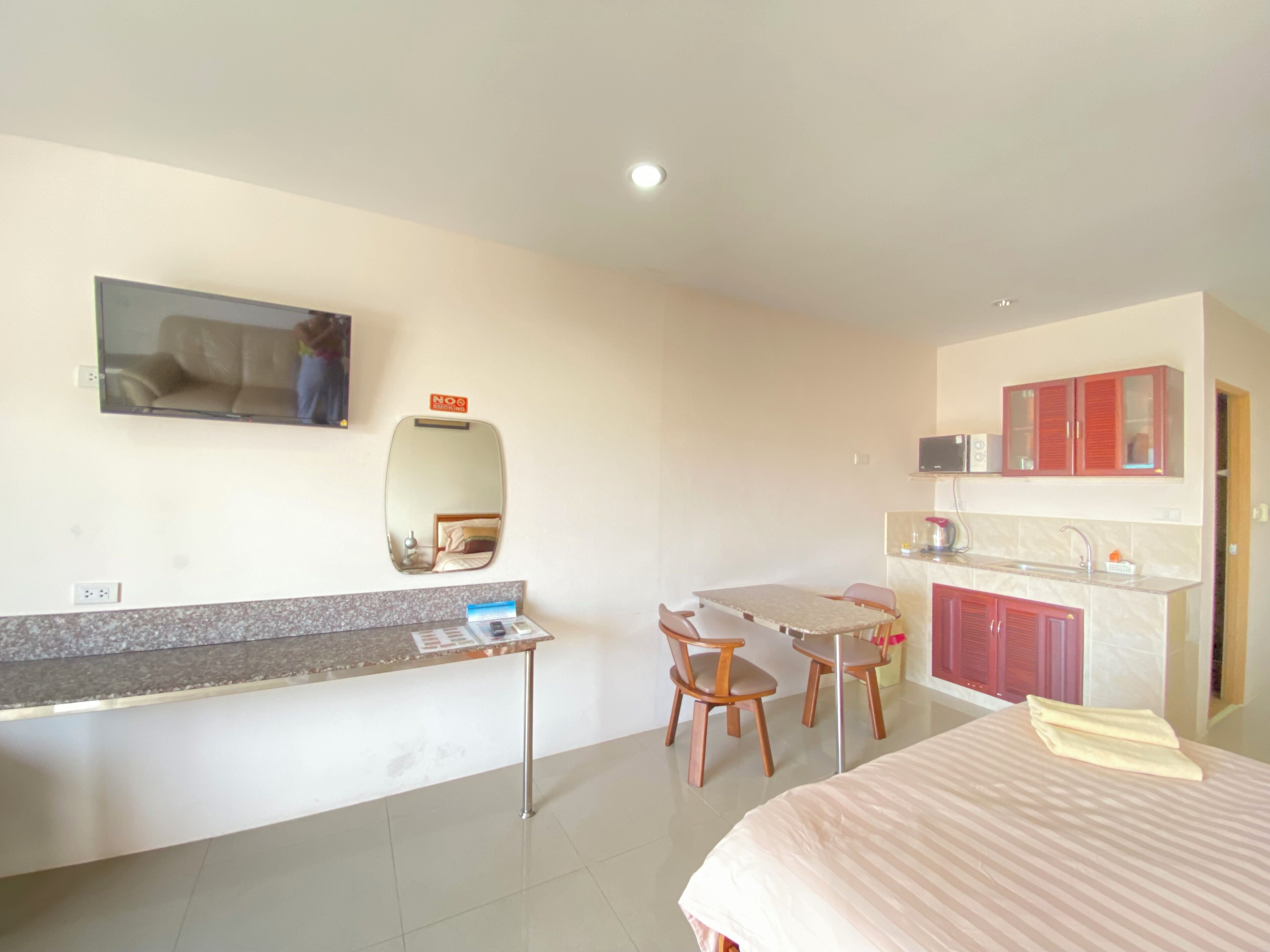 Habitación de hotel con cama, escritorio con silla, kitchenette pequeña y televisor montado en la pared.