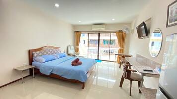 A hotel room with a bed, a desk, a chair, a TV, and a balcony with a view of buildings.
