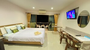 Habitación de hotel con cama, escritorio, silla, televisión y balcón con puerta de vidrio.