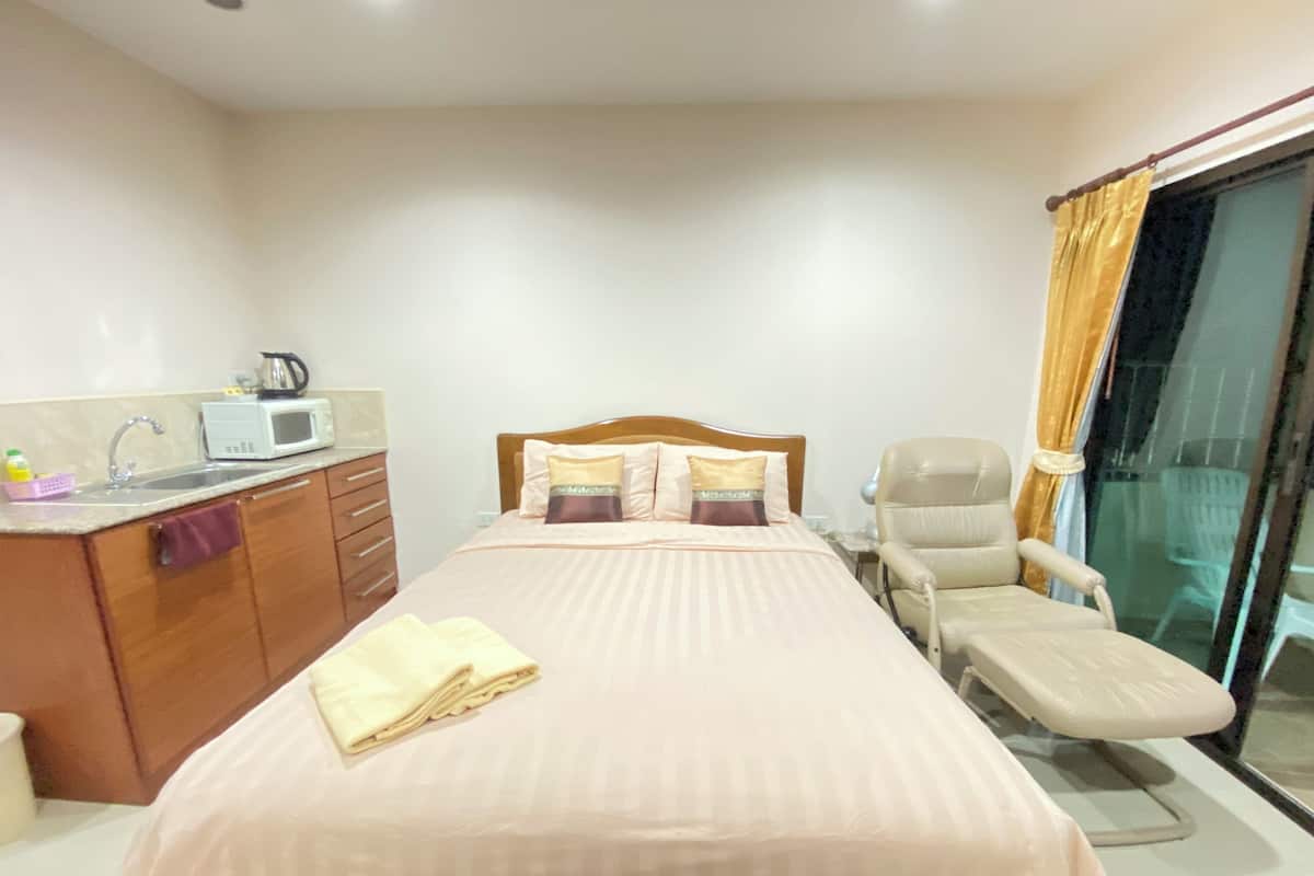 Un dormitorio con cama, una silla, un escritorio con microondas y una ventana con cortinas.