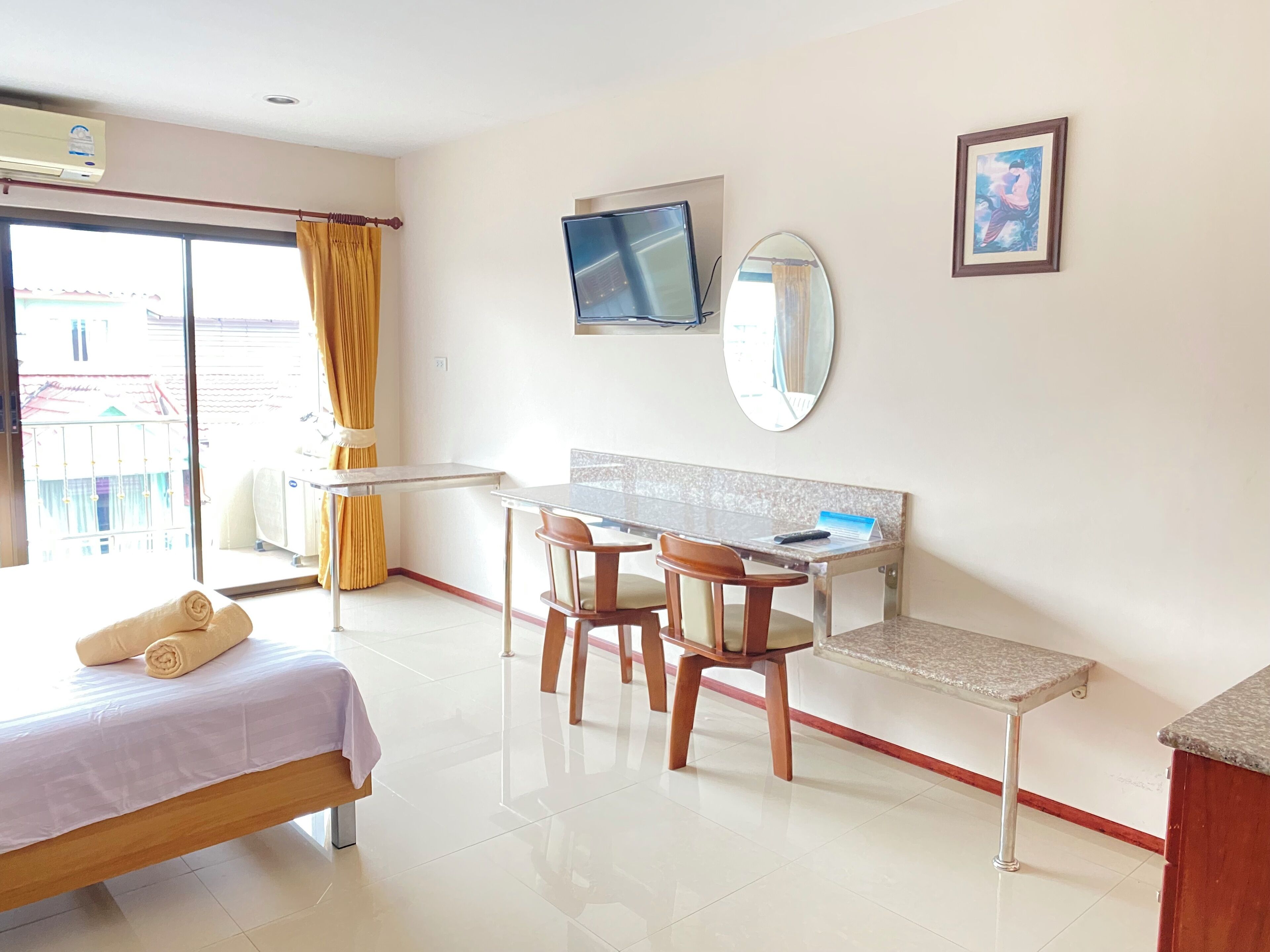 A hotel room with a bed, desk, chairs, a TV, a mirror, and a window with curtains.