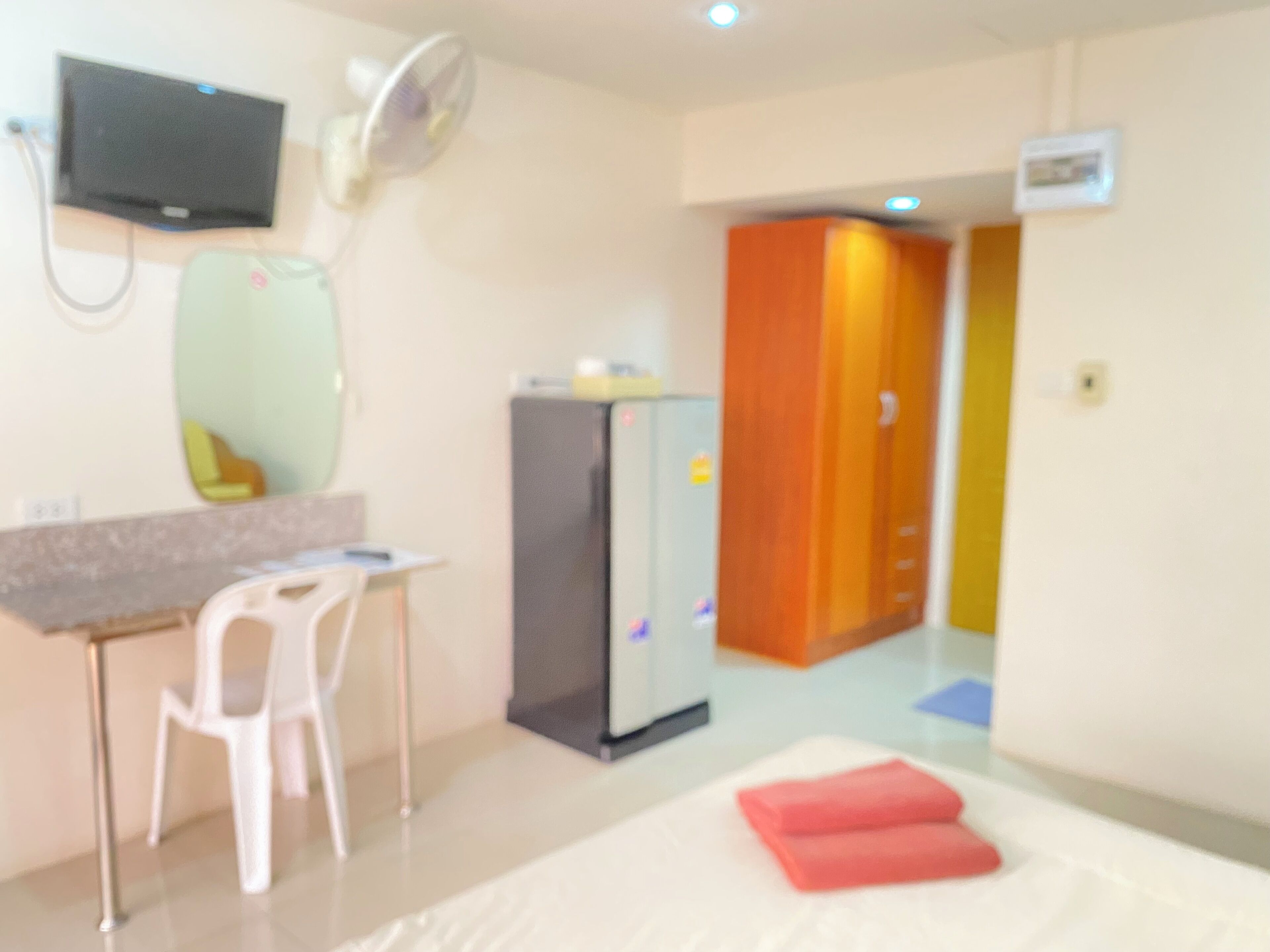 Habitación de hotel con cama, escritorio, silla, televisor, refrigerador y espejo.