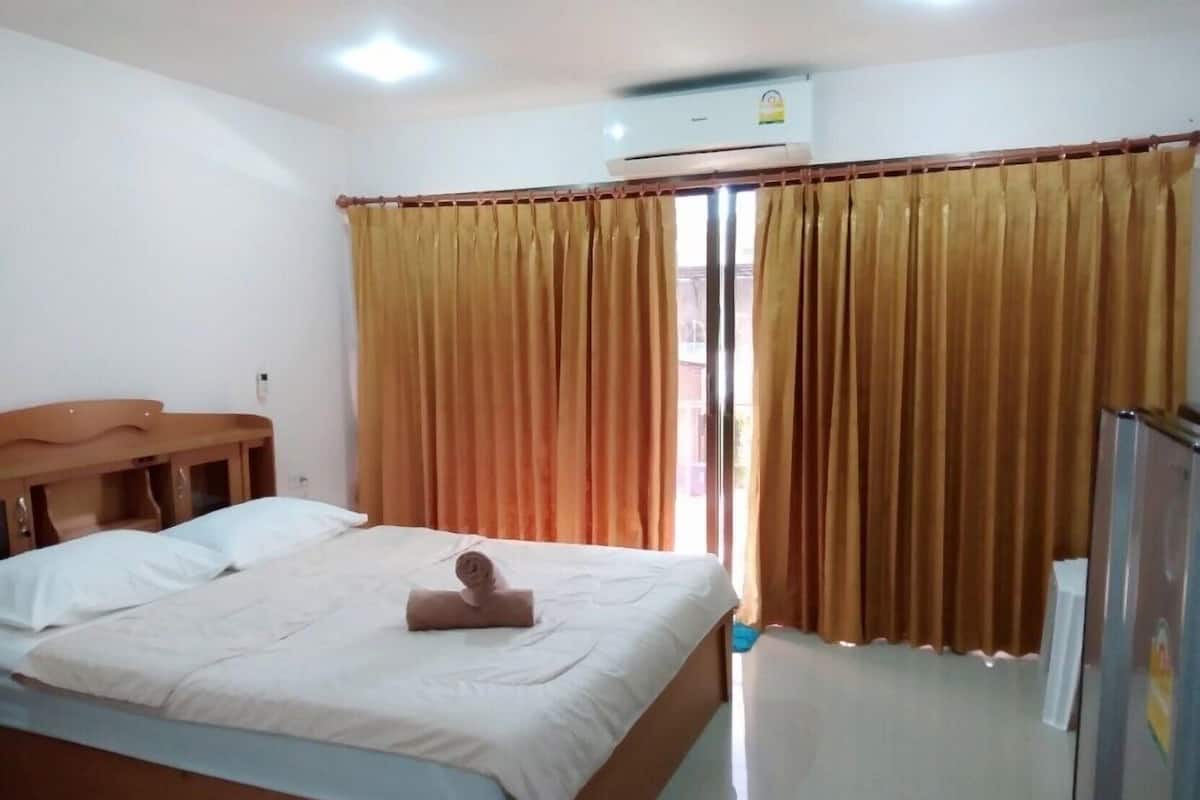 Una habitación de hotel con una cama, un banco de madera, aire acondicionado y cortinas.
