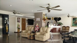 Amplia sala de estar con dos sofás color beige, una mesa de centro, una mesa de comedor con sillas, un ventilador de techo y una recepción con una planta.