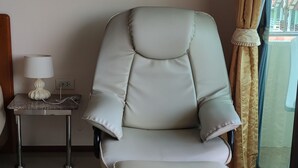 Una habitación moderna con un sillón de cuero blanco, una mesita con lámpara y vistas a través de un ventanal con cortinas.