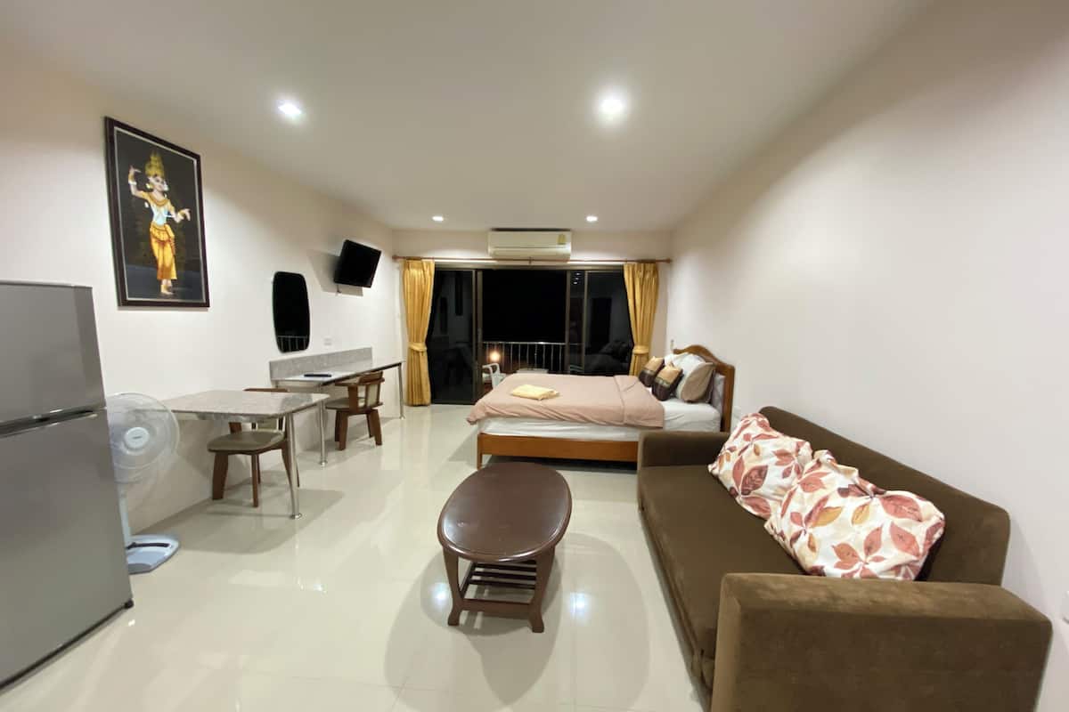 Una habitación de hotel moderna con una cama, un sofá, una mesa de comedor con sillas, una pequeña cocina y un televisor montado en la pared.