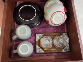 Una bandeja de madera con un paño púrpura, que contiene una tetera blanco y negro, una tetera blanca con detalles rojos, dos tazas de té y dos vasos de vidrio sobre una bandeja de madera con diseños plateados.