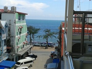 A street view with buildings, parked cars, and a view of the sea. - Dream Boutique Hotel (Cha-am)