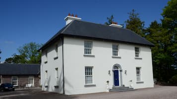 A two-story white building with a dark roof, a blue door, and a gravel driveway.