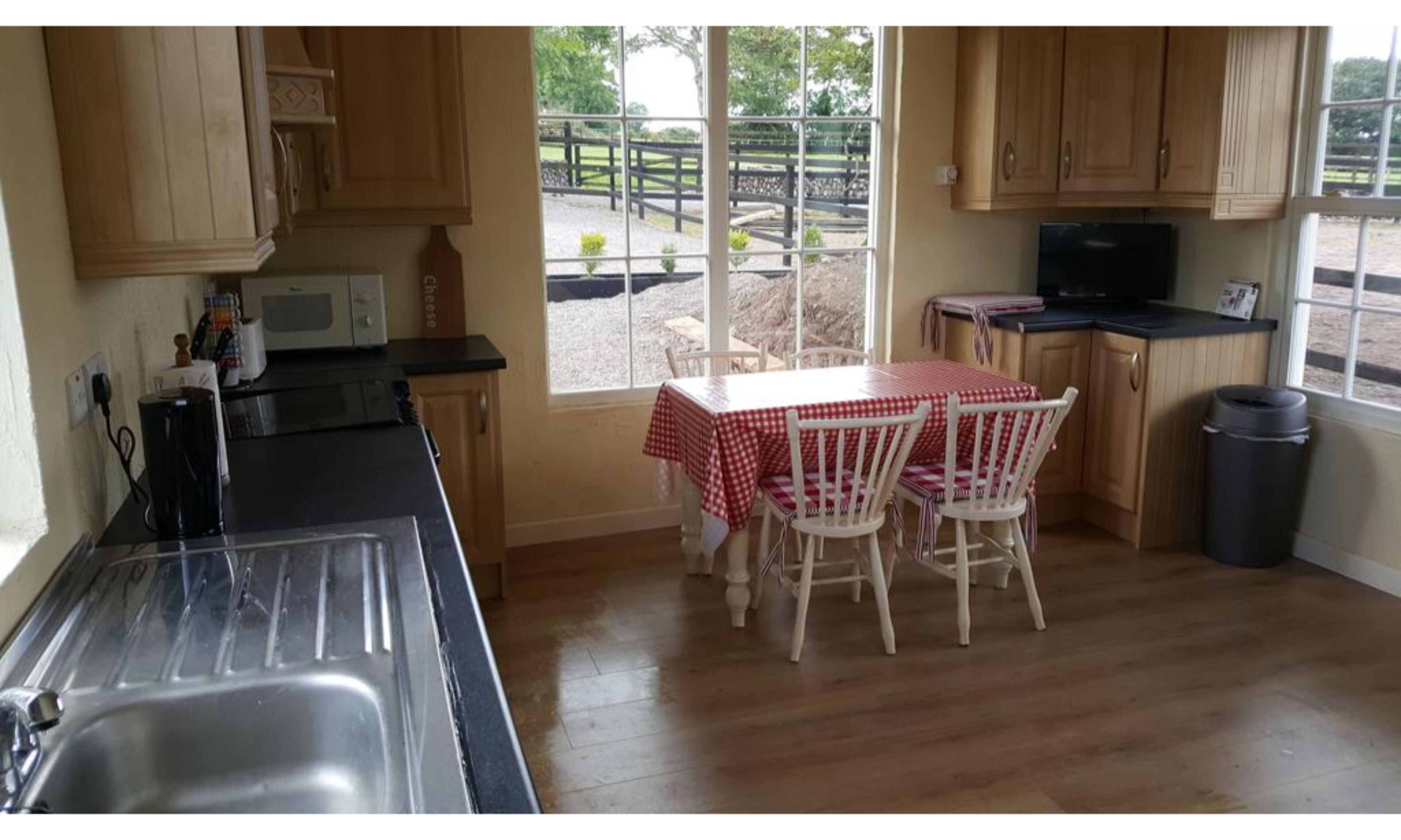 A kitchen with wooden cabinets, a black countertop, a sink, a table with a red and white checkered tablecloth, and chairs.