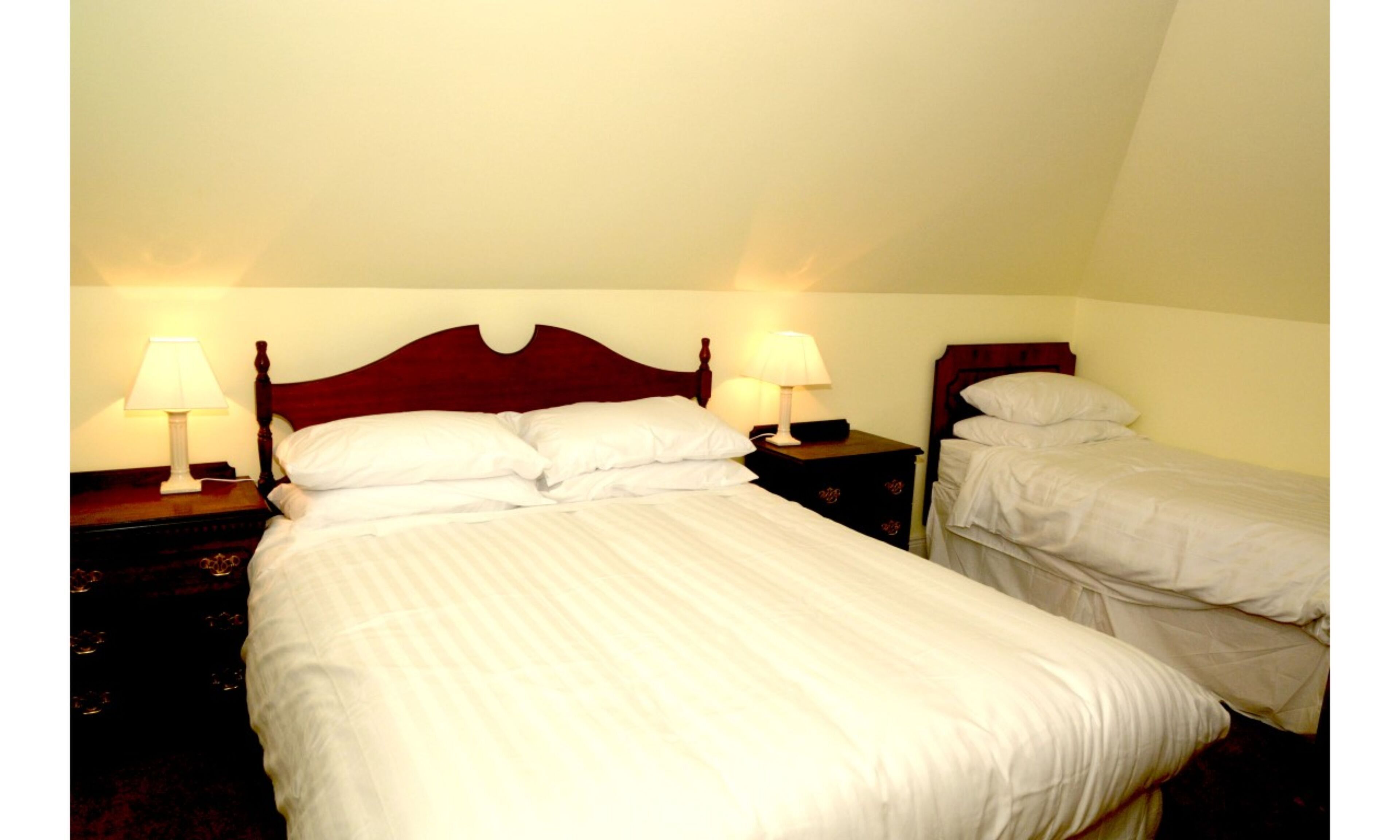 A hotel room with two single beds, each with a wooden headboard and bedside tables with lamps.